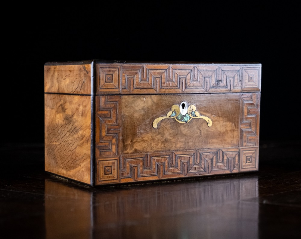 A rectangular walnut tea caddy featuring geometric parquetry borders, a mother-of-pearl escutcheon, and brass inlay on a dark wooden surface. View II