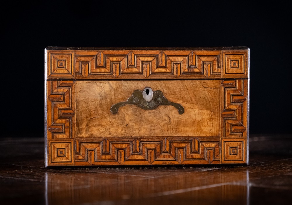 A rectangular walnut tea caddy featuring geometric parquetry borders, a mother-of-pearl escutcheon, and brass inlay on a dark wooden surface. View IV