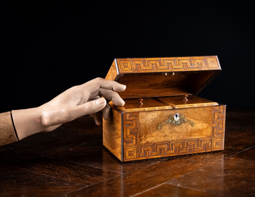 A rectangular walnut tea caddy featuring geometric parquetry borders, a mother-of-pearl escutcheon, and brass inlay on a dark wooden surface. View VII