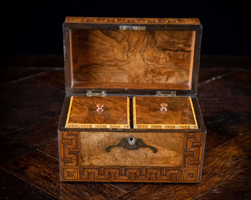 A rectangular walnut tea caddy featuring geometric parquetry borders, a mother-of-pearl escutcheon, and brass inlay on a dark wooden surface. View VIII