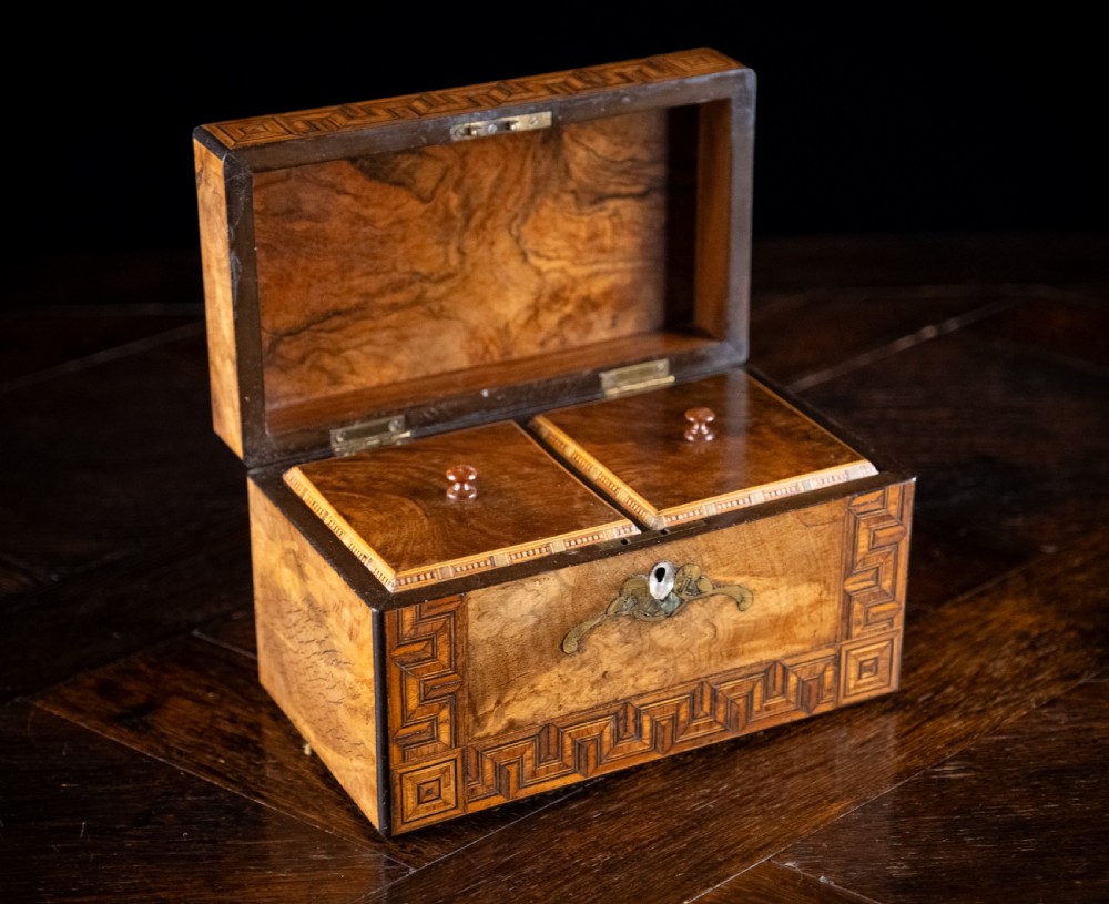 A rectangular walnut tea caddy featuring geometric parquetry borders, a mother-of-pearl escutcheon, and brass inlay on a dark wooden surface. View IX
