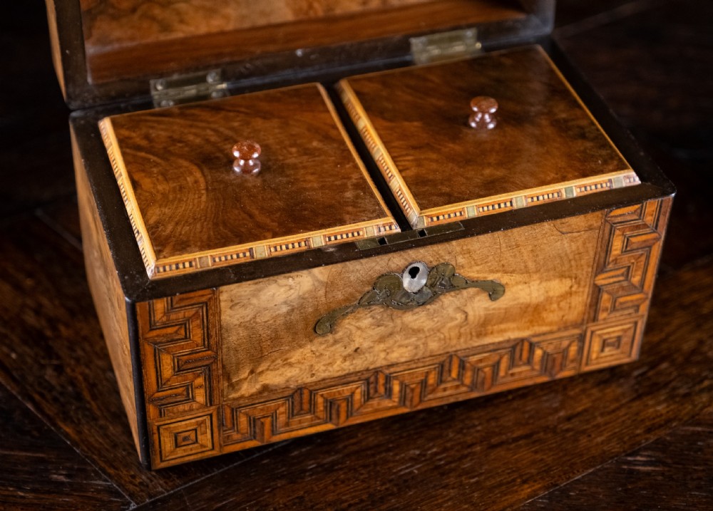 A rectangular walnut tea caddy featuring geometric parquetry borders, a mother-of-pearl escutcheon, and brass inlay on a dark wooden surface. View X