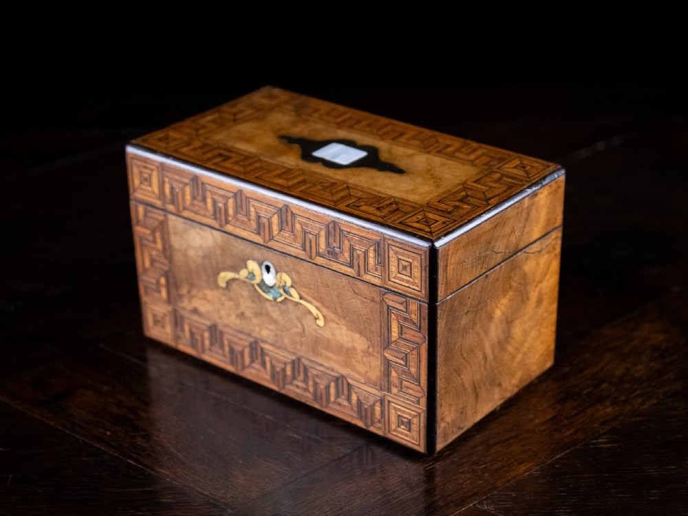 A rectangular walnut tea caddy featuring geometric parquetry borders, a mother-of-pearl escutcheon, and brass inlay on a dark wooden surface. View XIII