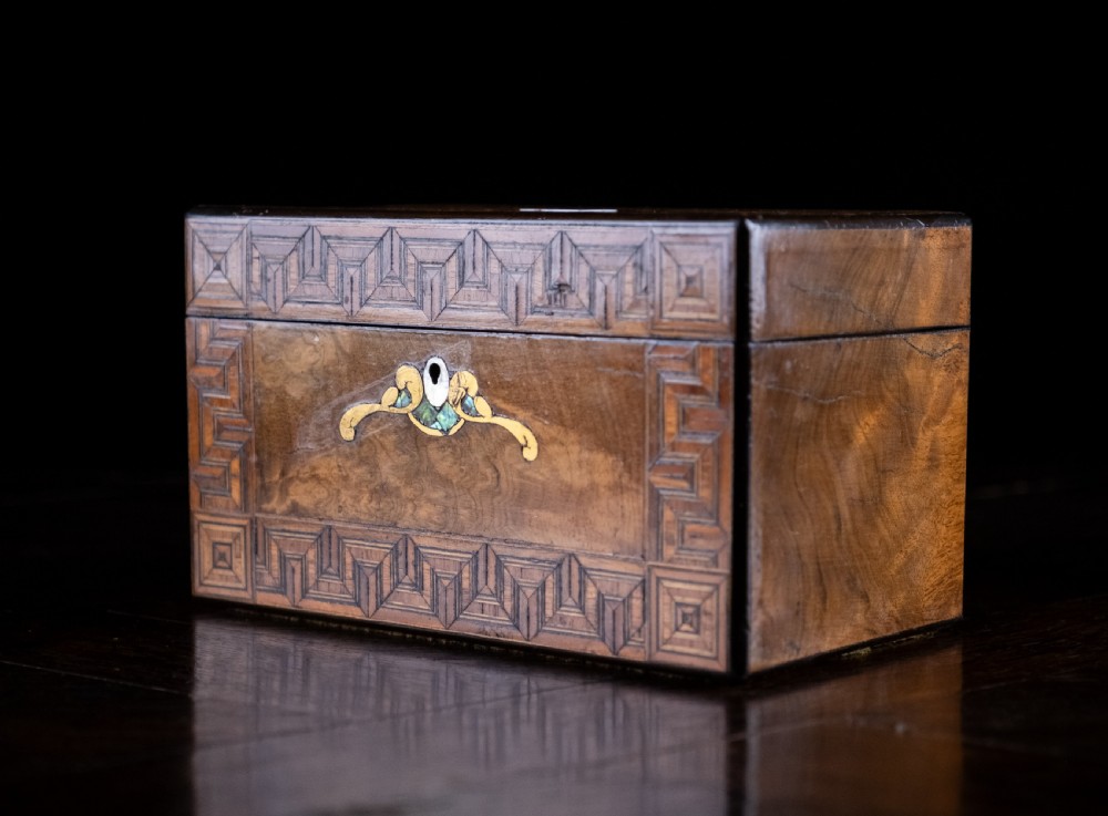 A rectangular walnut tea caddy featuring geometric parquetry borders, a mother-of-pearl escutcheon, and brass inlay on a dark wooden surface. View XIV