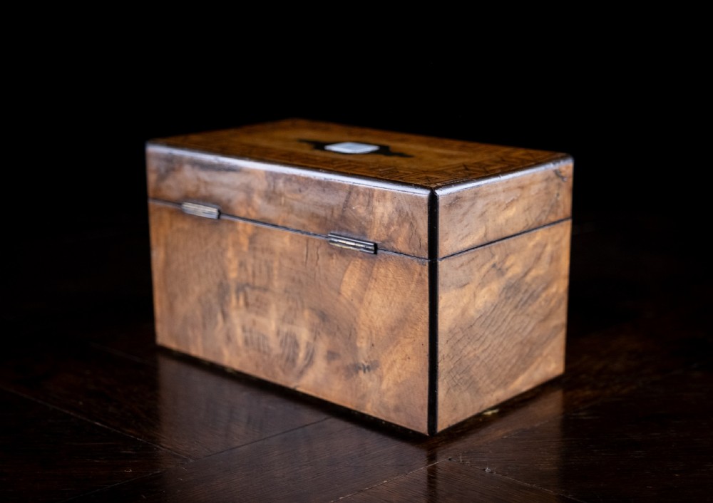 A rectangular walnut tea caddy featuring geometric parquetry borders, a mother-of-pearl escutcheon, and brass inlay on a dark wooden surface. View XVI