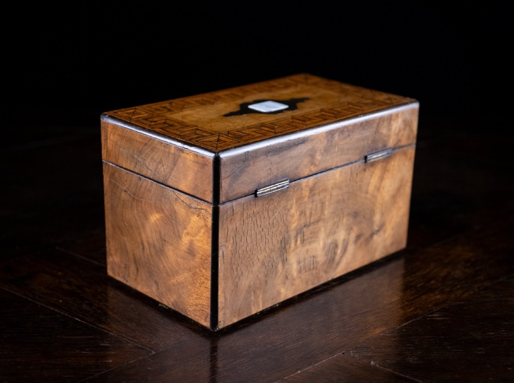 A rectangular walnut tea caddy featuring geometric parquetry borders, a mother-of-pearl escutcheon, and brass inlay on a dark wooden surface. View XVII