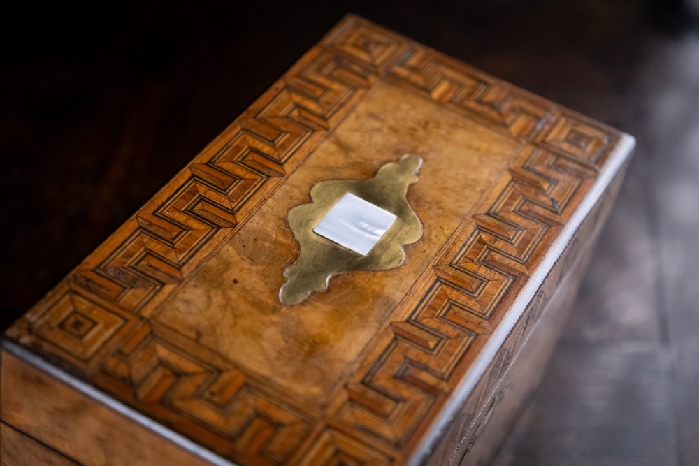 A rectangular walnut tea caddy featuring geometric parquetry borders, a mother-of-pearl escutcheon, and brass inlay on a dark wooden surface. View XVIII