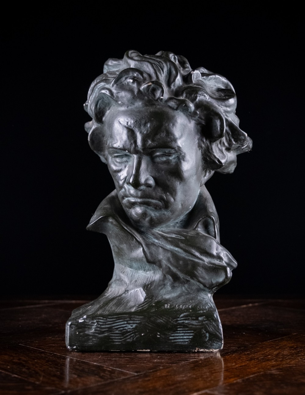 A dark bronze-coloured painted plaster bust depicting composer Ludwig van Beethoven with detailed hair and a dramatic collar on a square base.