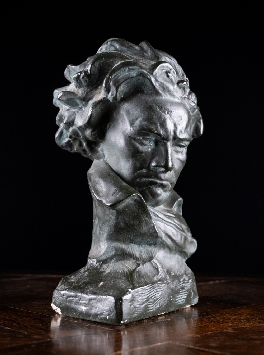 A dark bronze-coloured painted plaster bust depicting composer Ludwig van Beethoven with detailed hair and a dramatic collar on a square base. View V