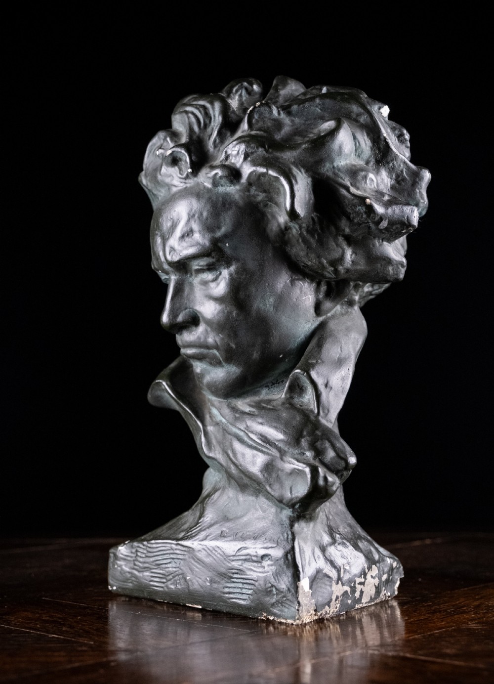 A dark bronze-coloured painted plaster bust depicting composer Ludwig van Beethoven with detailed hair and a dramatic collar on a square base. View X