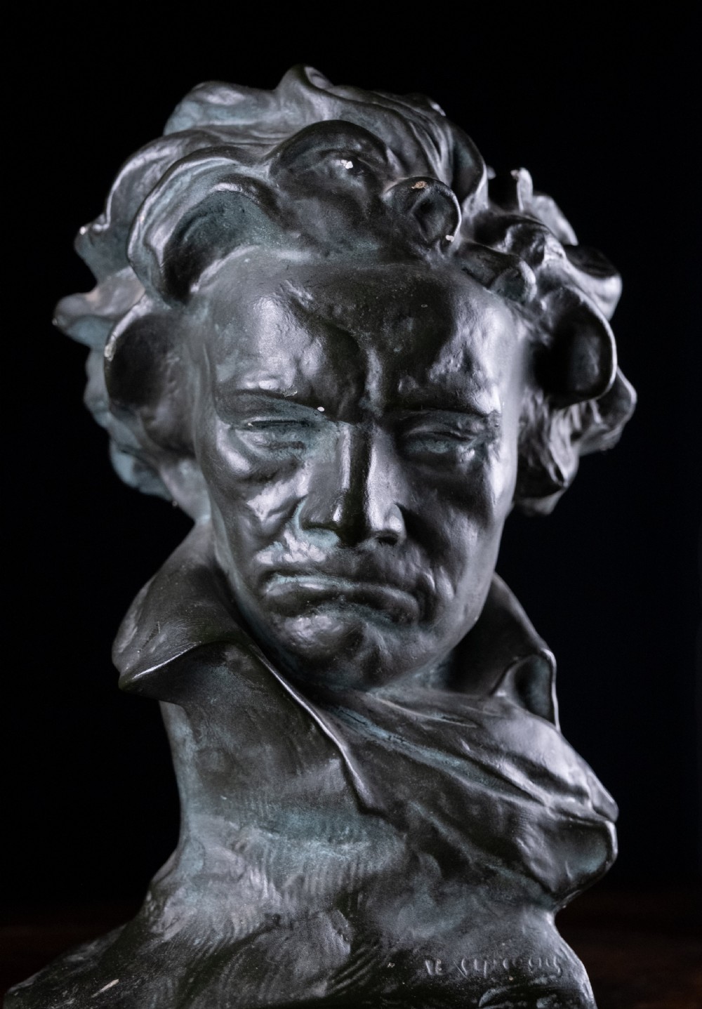 A dark bronze-coloured painted plaster bust depicting composer Ludwig van Beethoven with detailed hair and a dramatic collar on a square base. View XI
