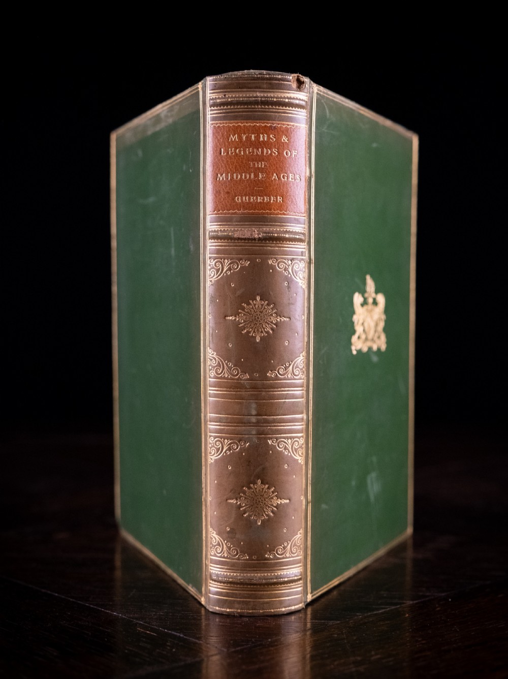 An upright antique book titled Myths and Legends of the Middle Ages with a brown leather spine featuring gilt tooling and green cloth covers.
