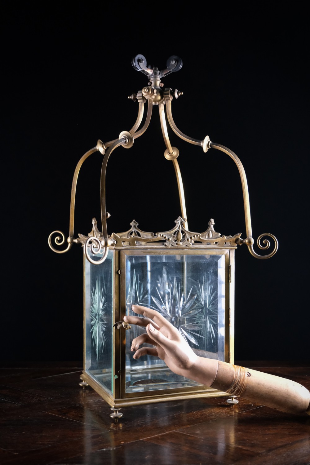 An Edwardian brass square-framed hall lantern featuring bevelled glass panels with starburst cuts and scrollwork hanging arms.