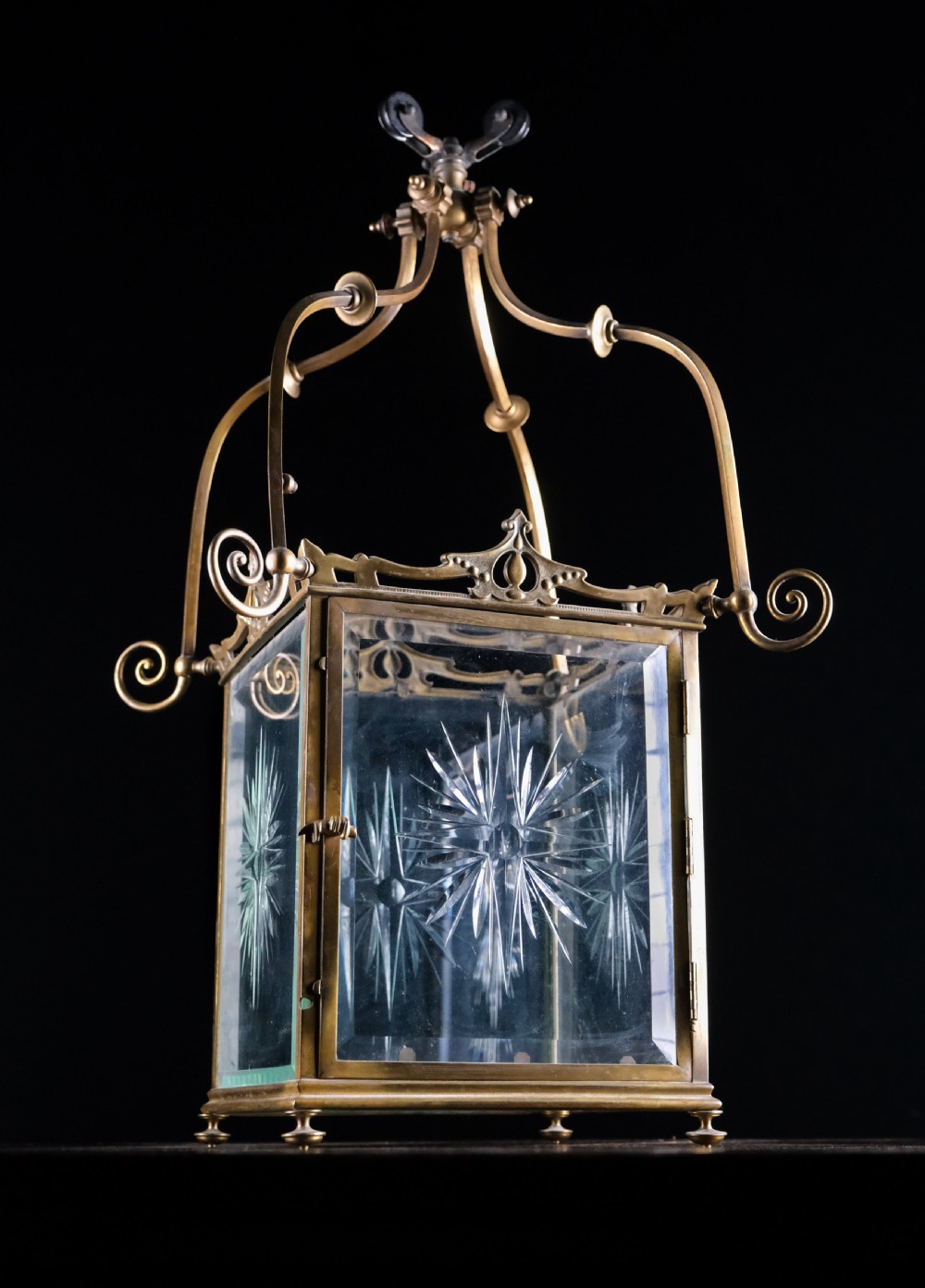 An Edwardian brass square-framed hall lantern featuring bevelled glass panels with starburst cuts and scrollwork hanging arms. View V