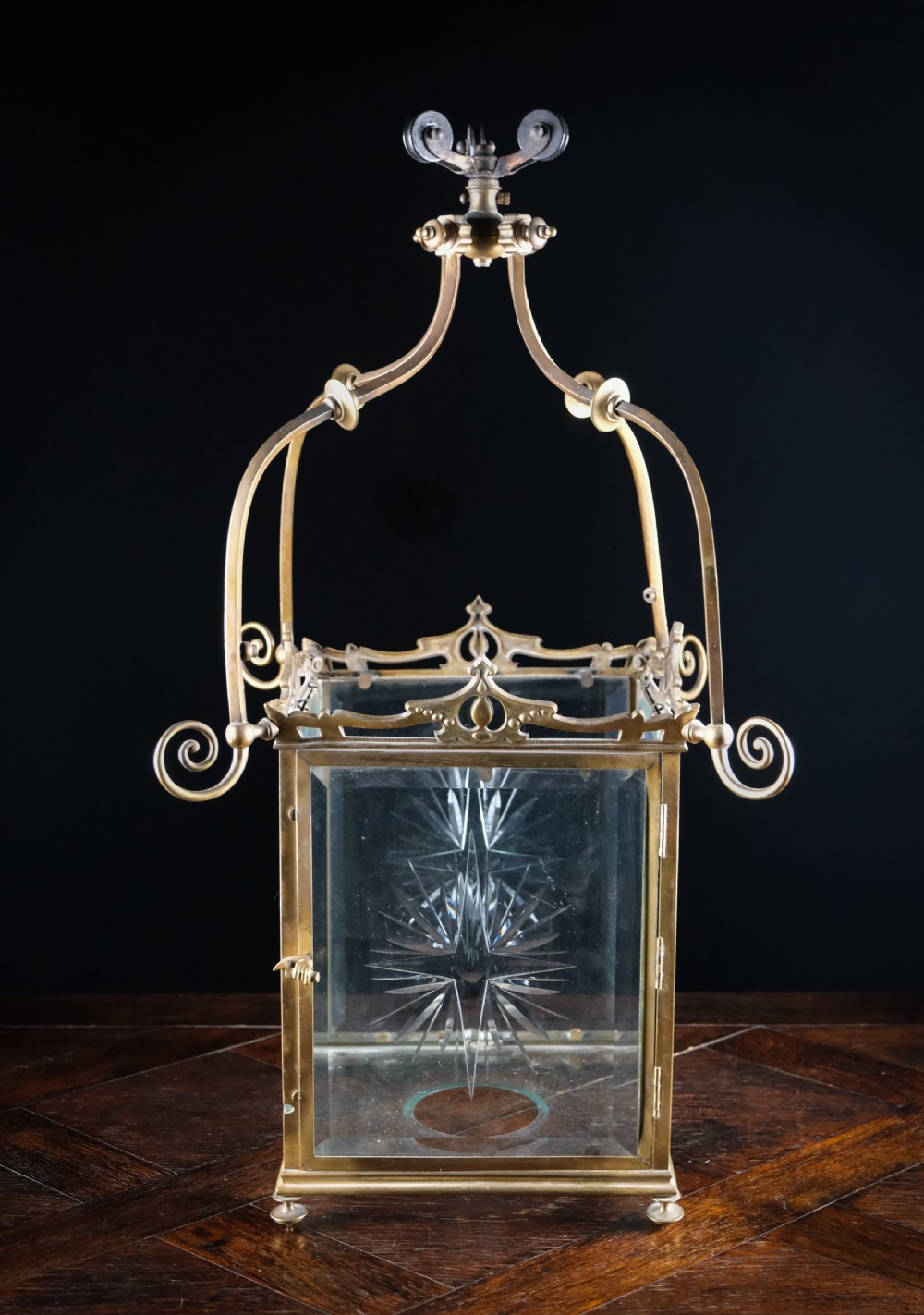 An Edwardian brass square-framed hall lantern featuring bevelled glass panels with starburst cuts and scrollwork hanging arms. View X