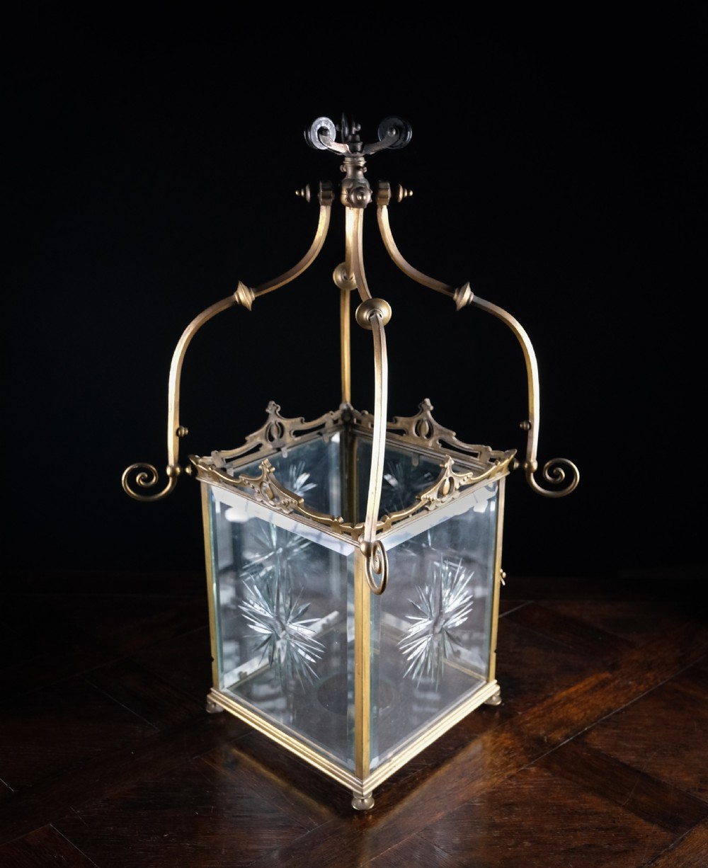 An Edwardian brass square-framed hall lantern featuring bevelled glass panels with starburst cuts and scrollwork hanging arms. View XII