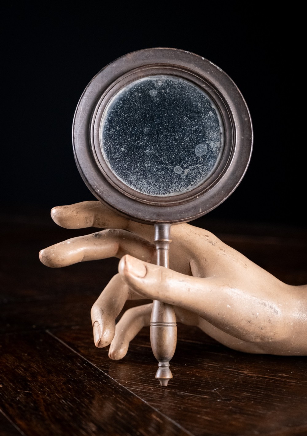 A circular Regency double-sided hand mirror with a turned dark timber frame, baluster handle, and aged mirror plate.