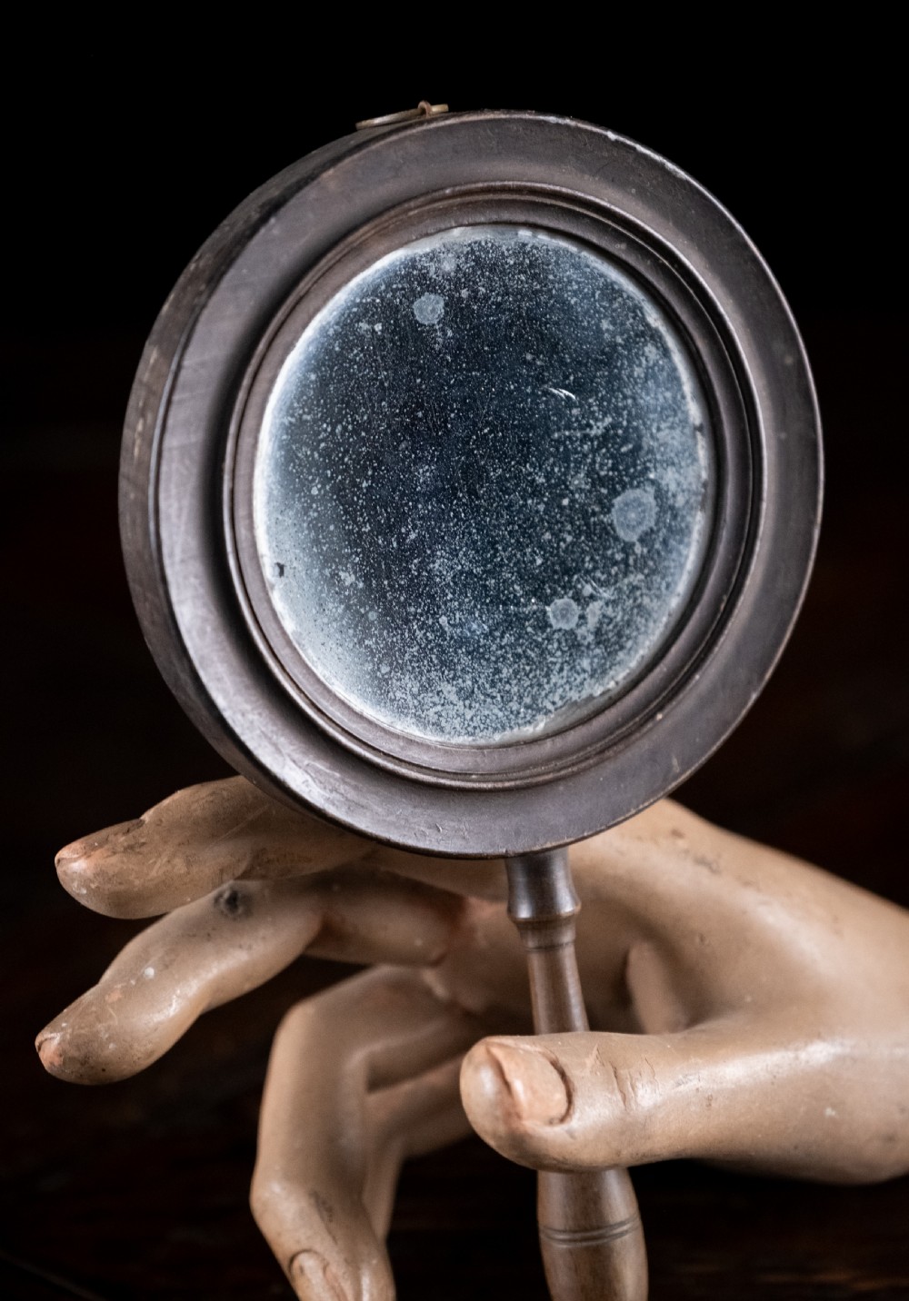 A circular Regency double-sided hand mirror with a turned dark timber frame, baluster handle, and aged mirror plate. View II