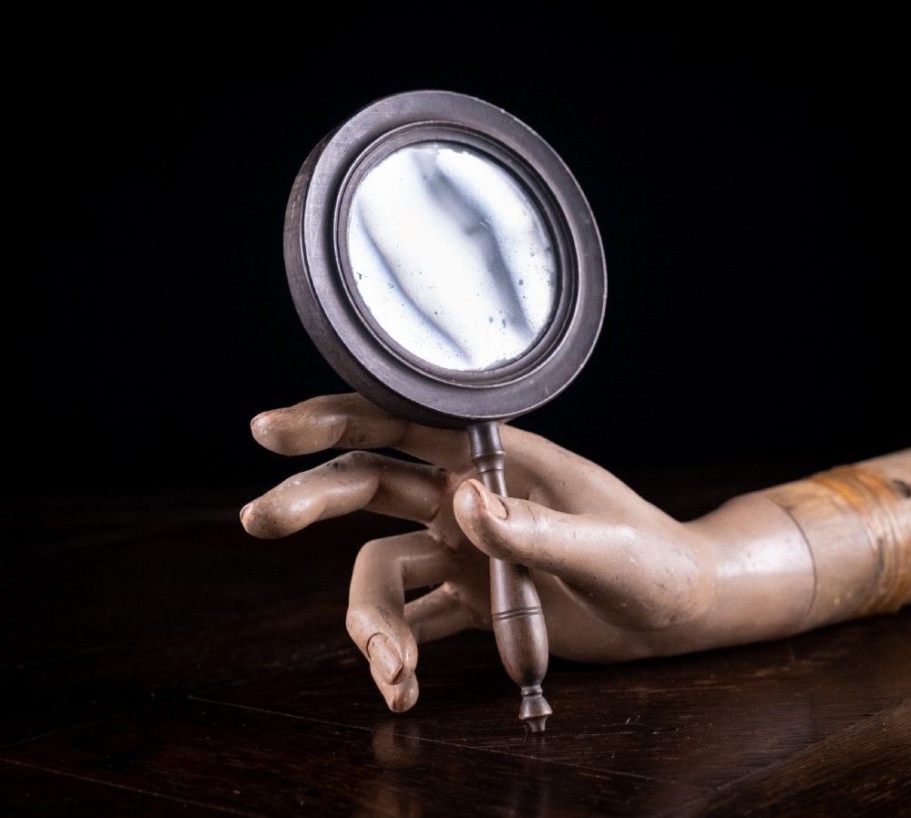 A circular Regency double-sided hand mirror with a turned dark timber frame, baluster handle, and aged mirror plate. View III
