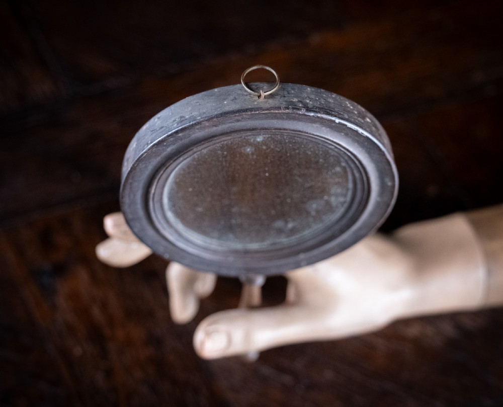 A circular Regency double-sided hand mirror with a turned dark timber frame, baluster handle, and aged mirror plate. View VII