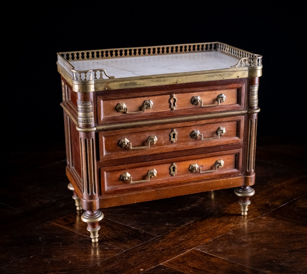 A miniature Louis XVI style mahogany three-drawer commode featuring brass mounts, fluted corner columns, and a gallery top inset with marble. View II