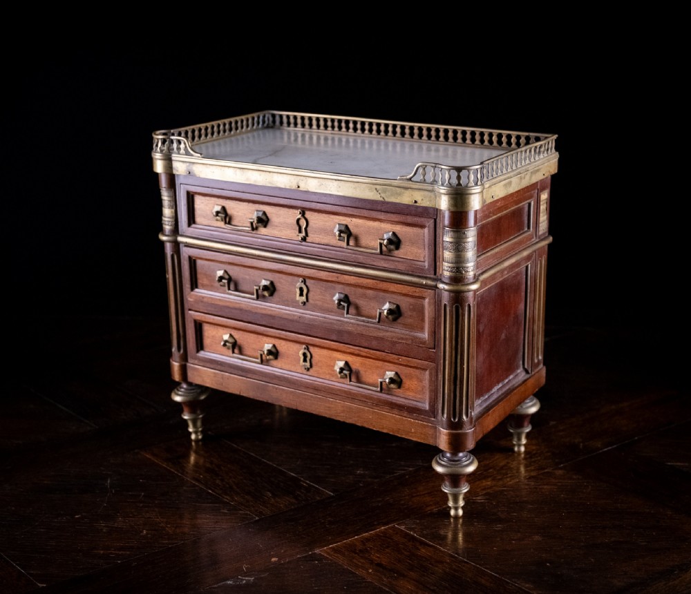 A miniature Louis XVI style mahogany three-drawer commode featuring brass mounts, fluted corner columns, and a gallery top inset with marble. View III