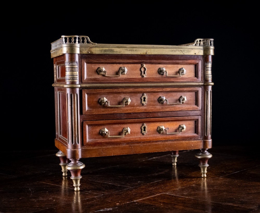A miniature Louis XVI style mahogany three-drawer commode featuring brass mounts, fluted corner columns, and a gallery top inset with marble. View V