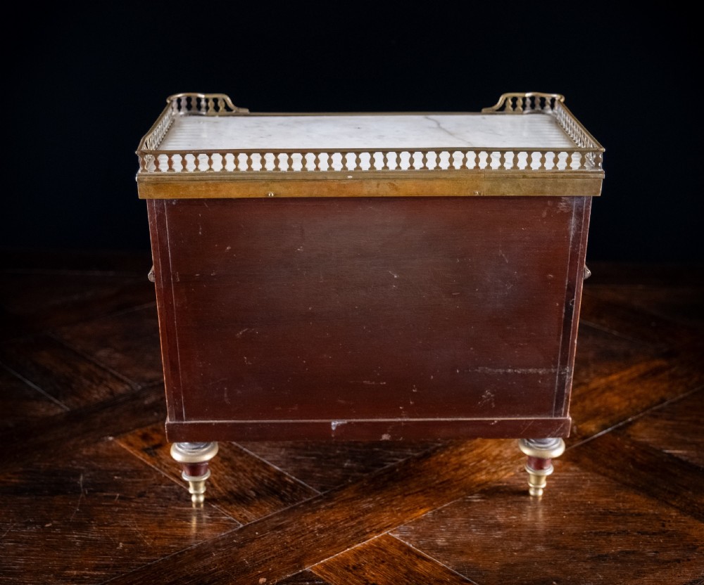 A miniature Louis XVI style mahogany three-drawer commode featuring brass mounts, fluted corner columns, and a gallery top inset with marble. View XVI