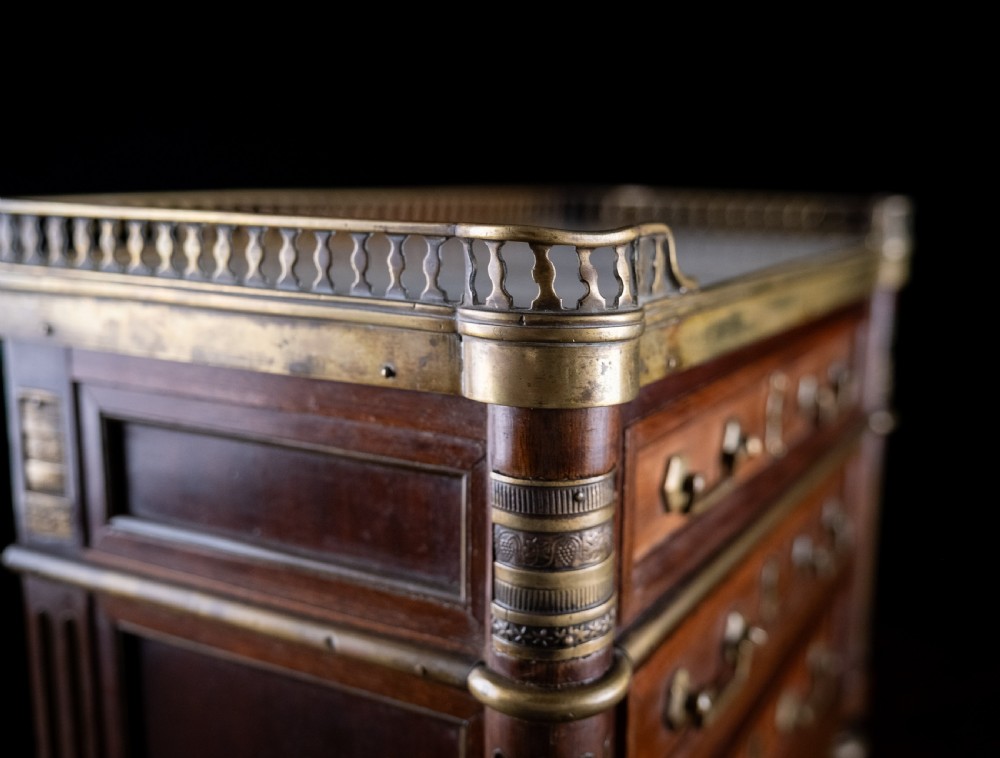 A miniature Louis XVI style mahogany three-drawer commode featuring brass mounts, fluted corner columns, and a gallery top inset with marble. View XXI