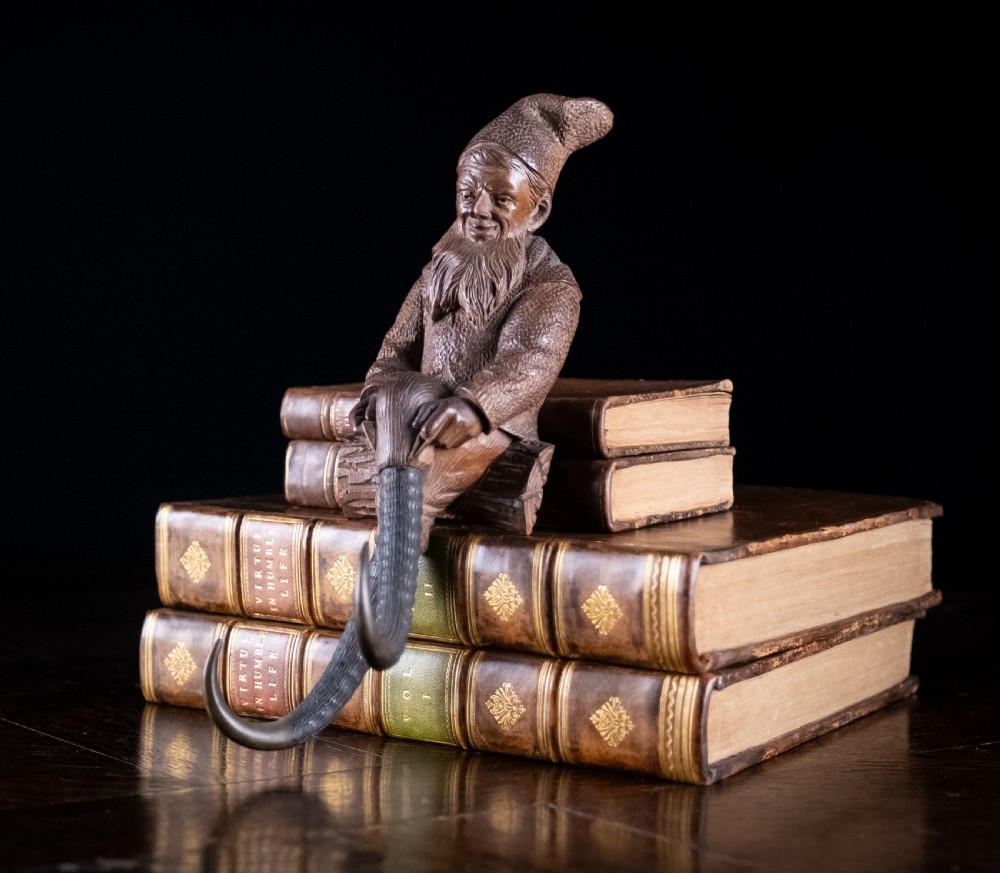 A dark carved wooden Black Forest gnome figure seated on a log with curved horn hooks extending as legs. View V