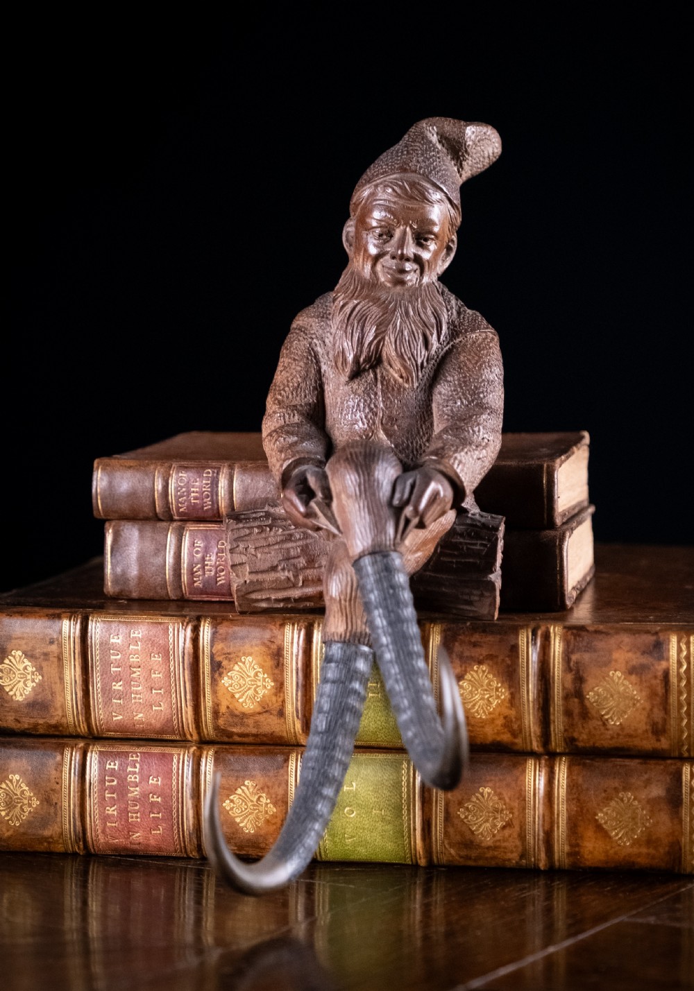 A dark carved wooden Black Forest gnome figure seated on a log with curved horn hooks extending as legs. View VI