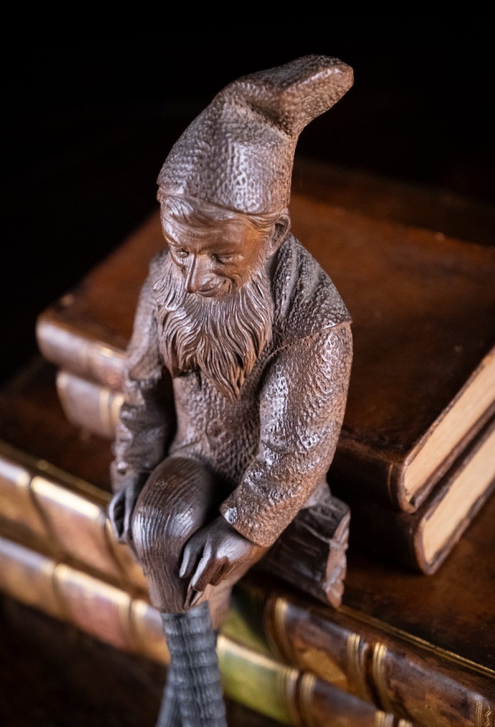 A dark carved wooden Black Forest gnome figure seated on a log with curved horn hooks extending as legs. View VIII