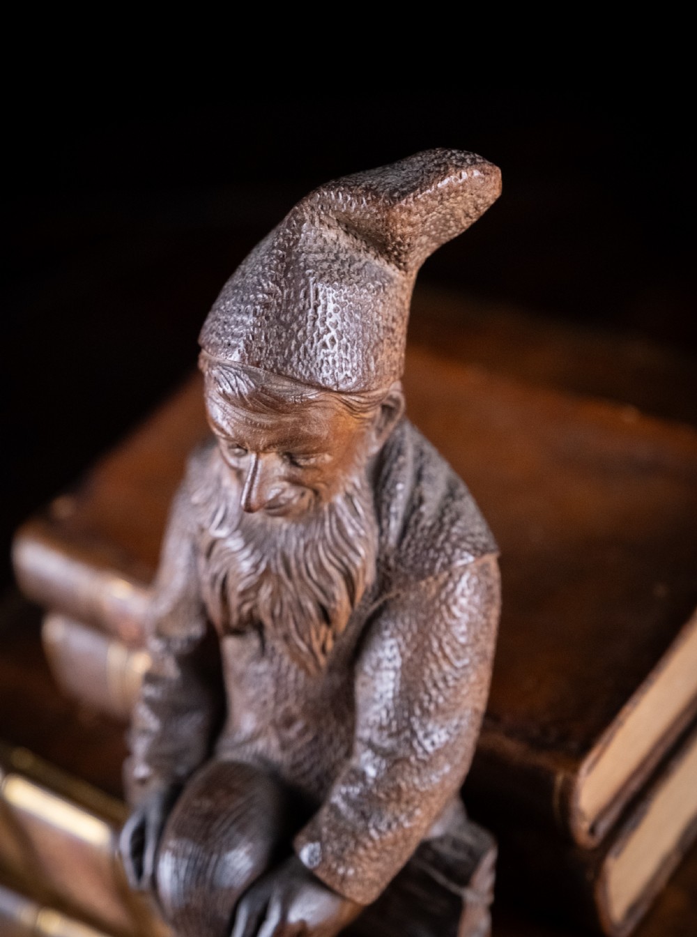 A dark carved wooden Black Forest gnome figure seated on a log with curved horn hooks extending as legs. View IX