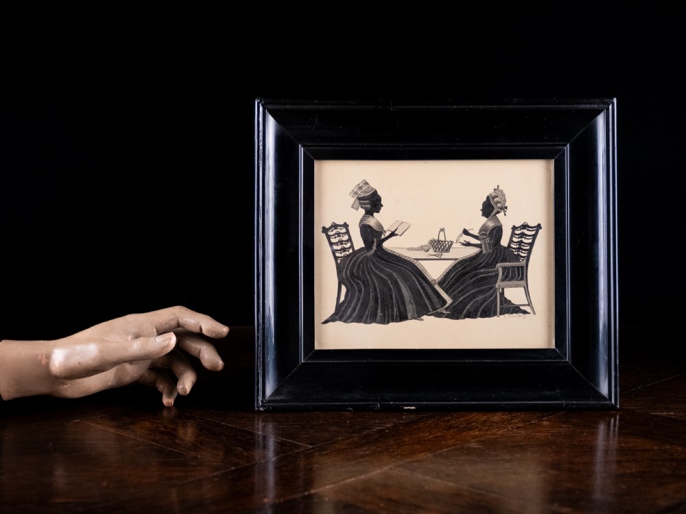 A framed 1837 silhouette artwork featuring two seated ladies in profile facing each other at a table, mounted within a wide black wooden frame. View V