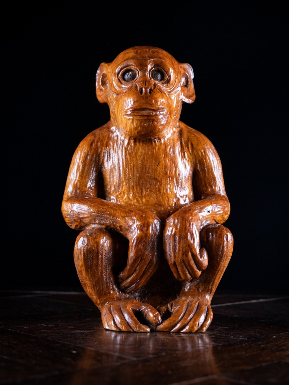 A hand-carved warm brown wooden sculpture depicting a seated monkey with chiselled fur details and dark eyes.
