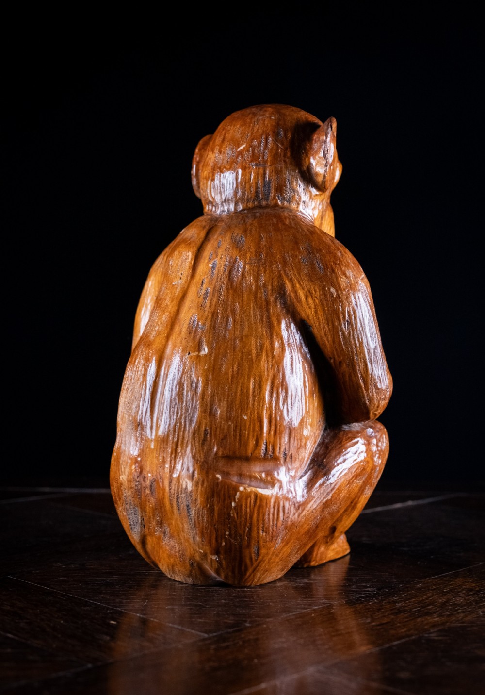 A hand-carved warm brown wooden sculpture depicting a seated monkey with chiselled fur details and dark eyes. View V