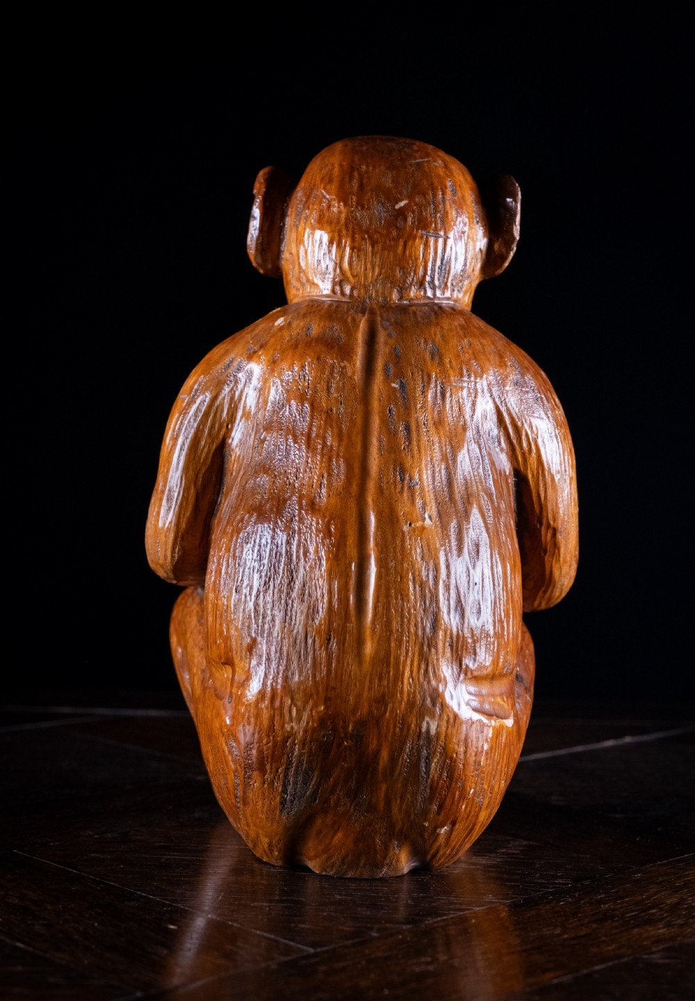 A hand-carved warm brown wooden sculpture depicting a seated monkey with chiselled fur details and dark eyes. View VI