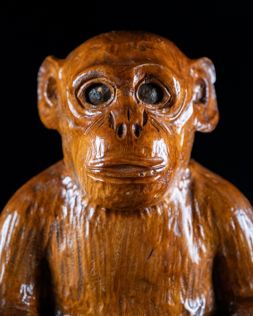 A hand-carved warm brown wooden sculpture depicting a seated monkey with chiselled fur details and dark eyes. View XI