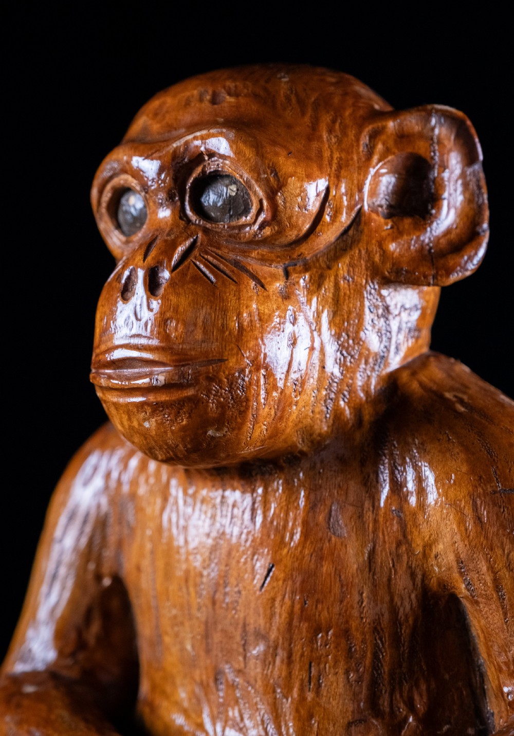 A hand-carved warm brown wooden sculpture depicting a seated monkey with chiselled fur details and dark eyes. View XII