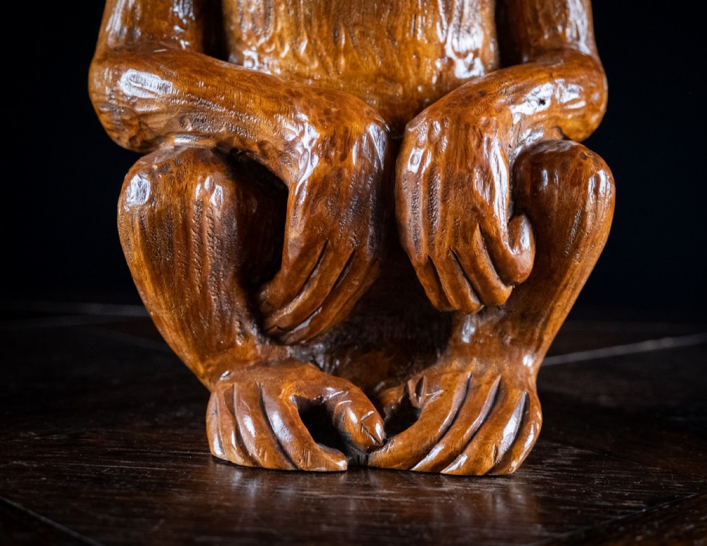 A hand-carved warm brown wooden sculpture depicting a seated monkey with chiselled fur details and dark eyes. View XIII