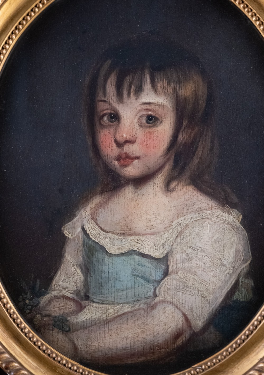 An 18th-century oval portrait painting depicting a young girl with brown hair wearing a blue and white dress within a gilded frame. View II