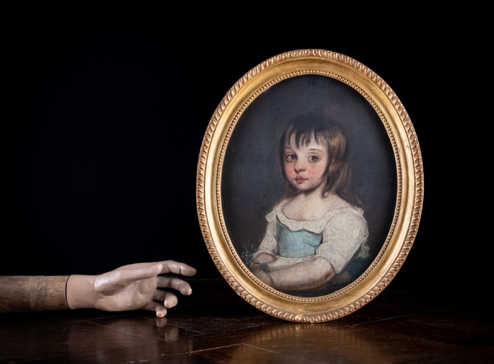 An 18th-century oval portrait painting depicting a young girl with brown hair wearing a blue and white dress within a gilded frame. View VI