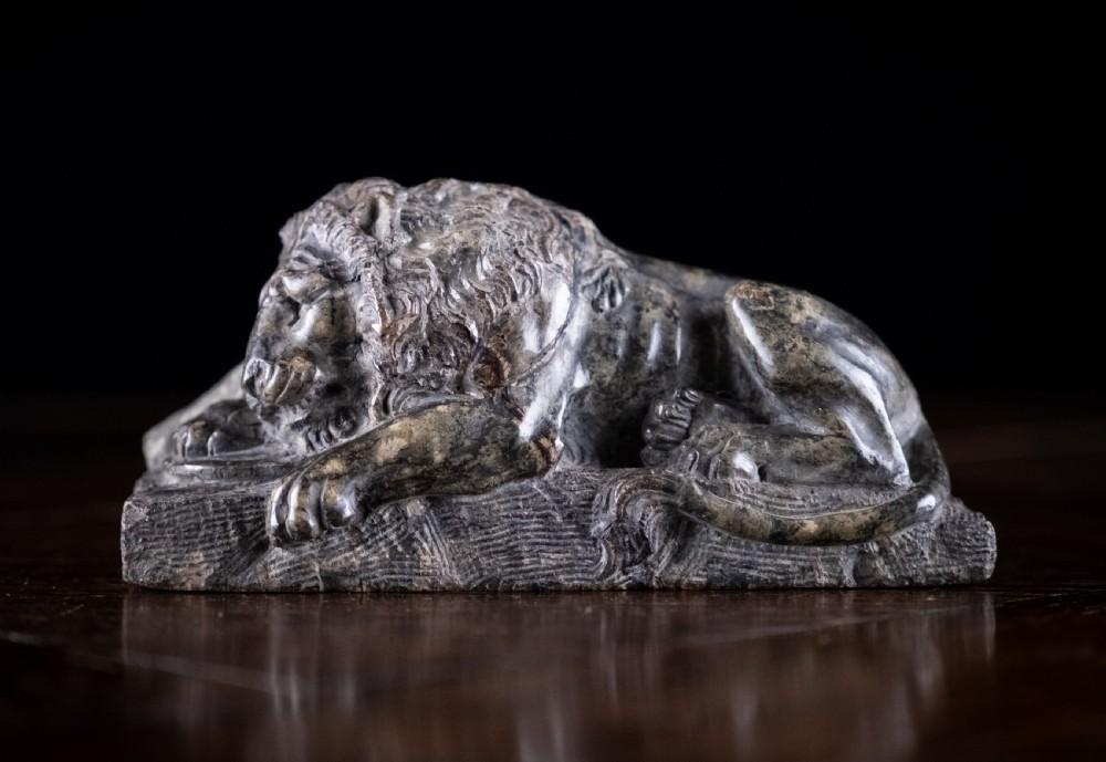 A carved dark serpentine stone sculpture depicting the recumbent Lion of Lucerne resting on an integral rectangular stone base.