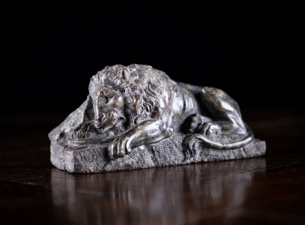 A carved dark serpentine stone sculpture depicting the recumbent Lion of Lucerne resting on an integral rectangular stone base. View II