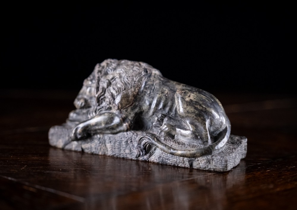 A carved dark serpentine stone sculpture depicting the recumbent Lion of Lucerne resting on an integral rectangular stone base. View V