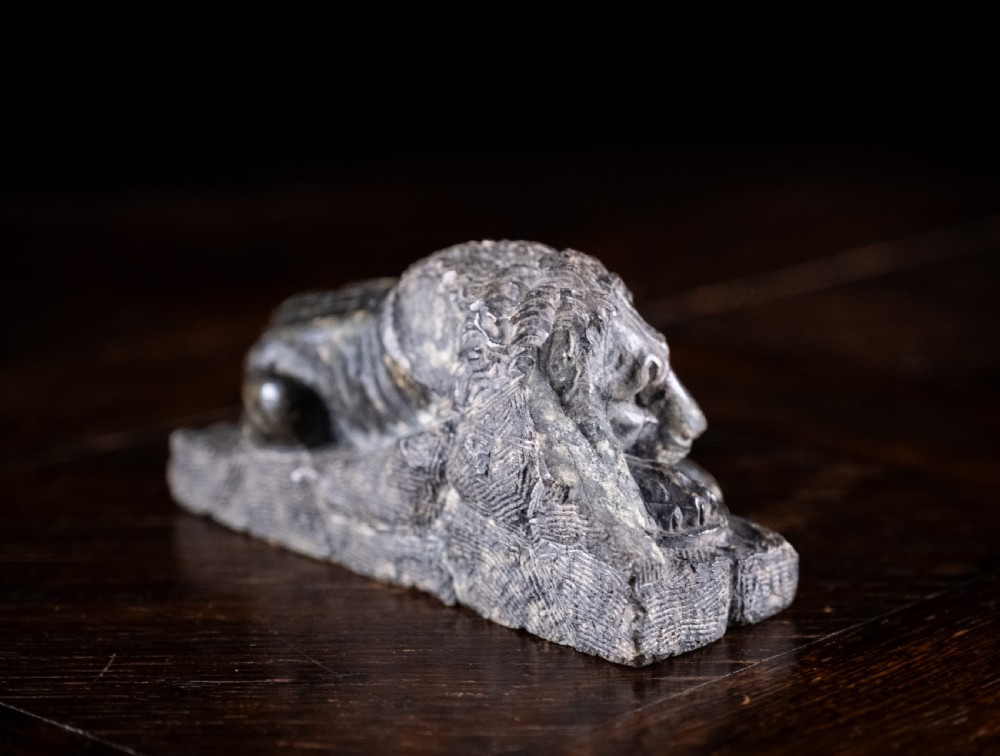 A carved dark serpentine stone sculpture depicting the recumbent Lion of Lucerne resting on an integral rectangular stone base. View VII