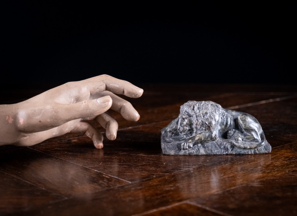 A carved dark serpentine stone sculpture depicting the recumbent Lion of Lucerne resting on an integral rectangular stone base. View X
