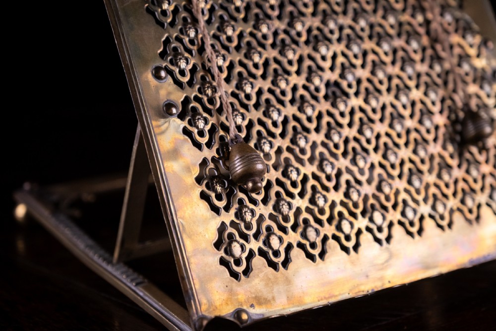 An antique brass folding book rest featuring an intricate pierced fretwork pattern, adjustable easel backing, and weighted page holder cords. View III