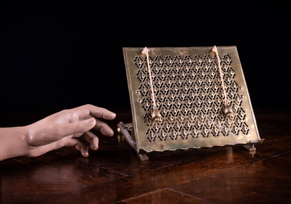 An antique brass folding book rest featuring an intricate pierced fretwork pattern, adjustable easel backing, and weighted page holder cords. View IV