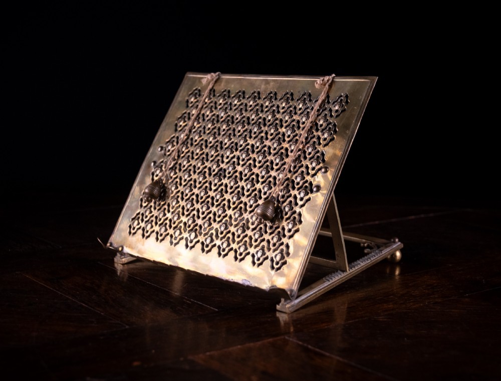 An antique brass folding book rest featuring an intricate pierced fretwork pattern, adjustable easel backing, and weighted page holder cords. View V